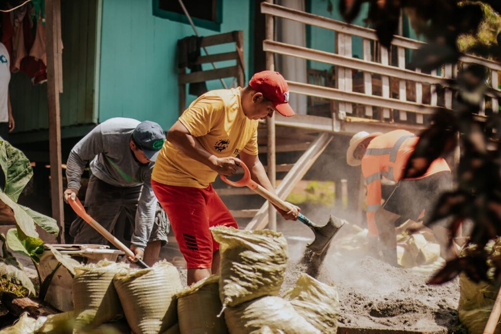 Men working energetically on construction, shoveling sand into bags outdoors.